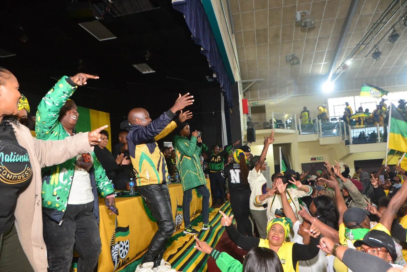 People on the platform and in the crowd raise their hands inside the hall.