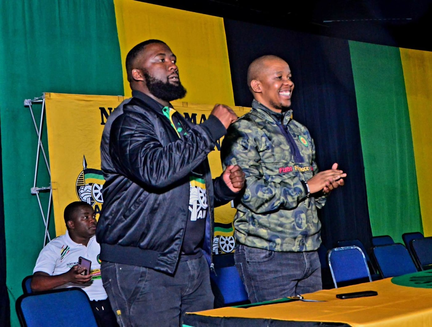 Two participants stand at the platform, one raising a fist and the other clapping.