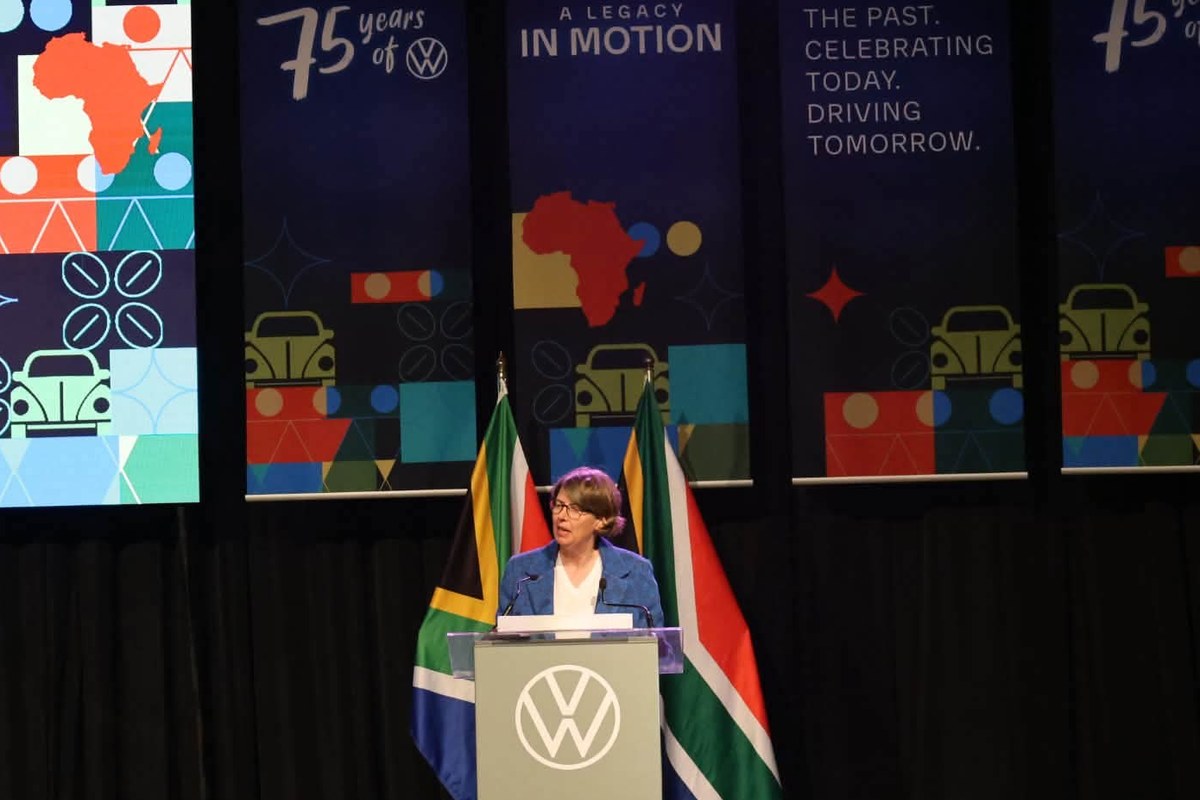 Volkswagen Group Africa chairperson Martina Biene speaking at the gala dinner stage, with the 75 years of Volkswagen and A Legacy in Motion stage panels behind her and South African flags beside the podium
