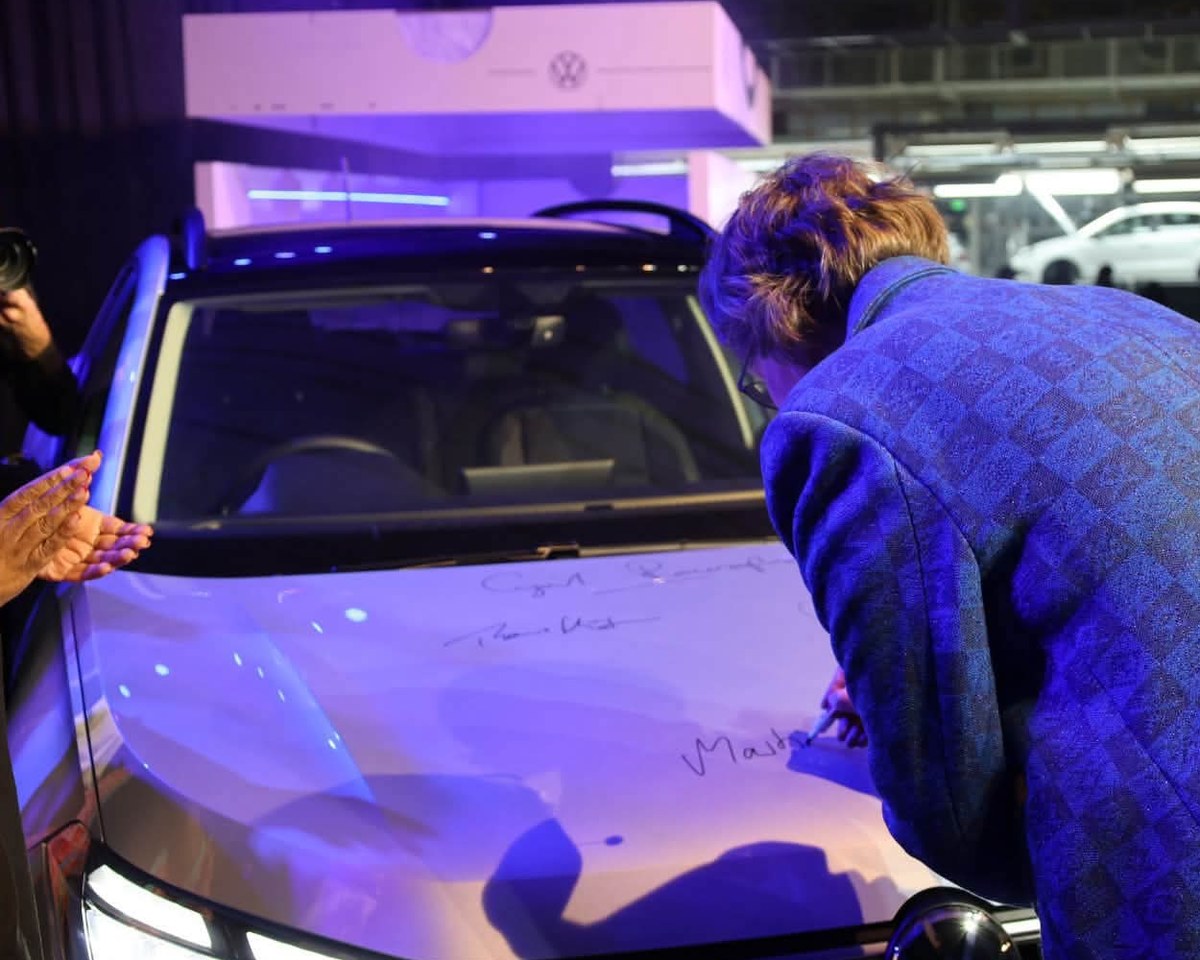Martina Biene signing the bonnet of the newly unveiled Volkswagen Tengo bearing the signatures of President Cyril Ramaphosa and Thomas Schäfer, with the Kariega production hall visible behind